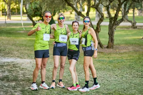 Cuatro corredores sonríen, listos para las carreras populares Zaragoza. Llevan camisetas verdes con dorsales y gafas de sol.