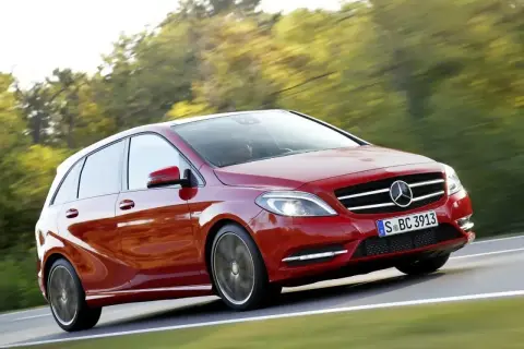 Czerwony Mercedes B Klasa pędzi po drodze, otoczony zielenią drzew.