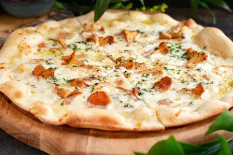Pyszna pizza z kurkami, rozpływającym się serem i ziołami, podana na drewnianej desce.