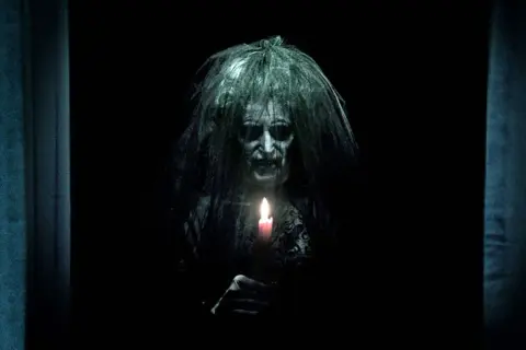 Przerażająca postać z zapaloną świecą, zapowiedź najstraszniejszych horrorów z jumpscare.
