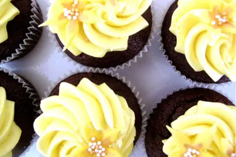 Chokladmuffins med fluffig gul frosting, dekorerade med små blommor och pärlor. Perfekt frosting till chokladmuffins!