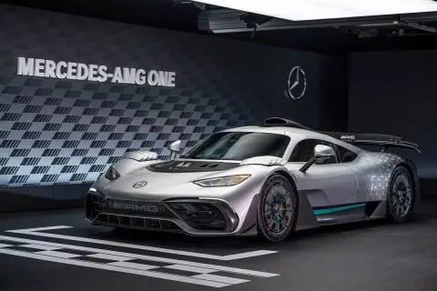 Srebrny Mercedes-AMG ONE, hiperauto z elementami wyścigowymi, prezentuje się na tle ściany z logo i napisem "MERCEDES-AMG ONE".