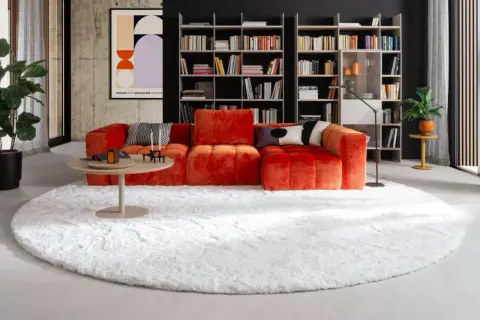 Ein flauschiger weißer Teppich bildet die Basis für das orangefarbene Sofa. So lässt sich der Teppich unter dem Sofa richtig platzieren.