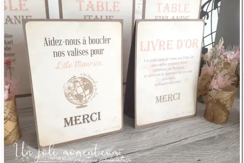 Un **livre** d'or et une carte "Aidez-nous à boucler nos valises pour l'Île Maurice" sur une table en bois, décorés de fleurs séchées.