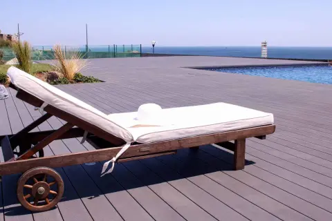 Tumbona lista para el sol sobre una terraza de madera composite, con piscina y mar al fondo.