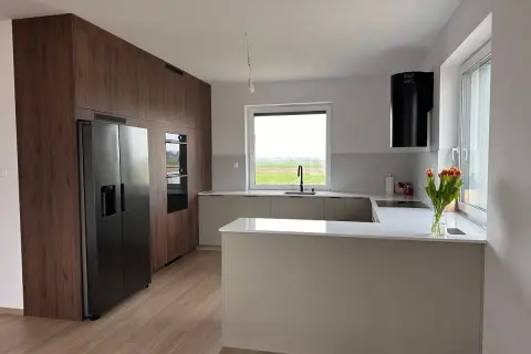 Nowoczesna kuchnia z zabudową w drewnie, wyspą i czarnym okapem. Idealne miejsce na przygotowanie dań haute cuisine.