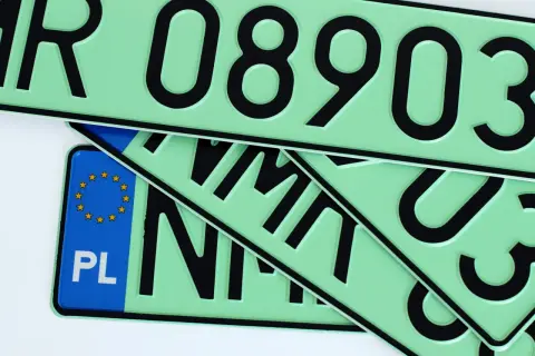 Kilka zielonych tablic rejestracyjnych z czarnymi numerami i literami, jedna z nich ma niebieski pasek z gwiazdkami UE i napisem PL.
