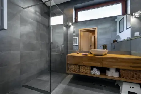 Salle de bain moderne avec douche à l'italienne, carrelage gris, meuble en bois, vasque et miroir. L'étanchéité de la douche italienne est assurée par un receveur discret.