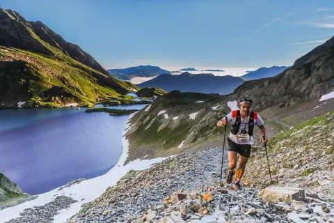 Un coureur de trail, le **vo2 max** à son apogée, grimpe un sentier rocailleux près de lacs de montagne bleus sous un ciel clair.