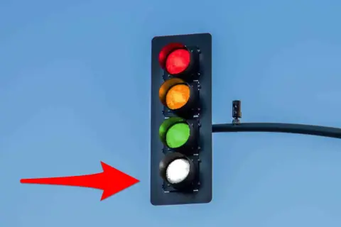 Un feu de circulation avec les lumières rouge, orange et verte allumées, et la lumière blanche clignotante. Une flèche rouge pointe vers le feu.