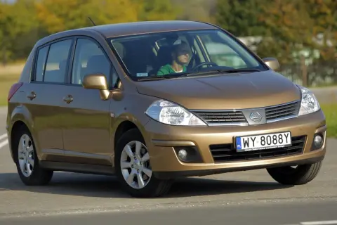 Złoty Nissan Tiida z mężczyzną za kierownicą jedzie po drodze.