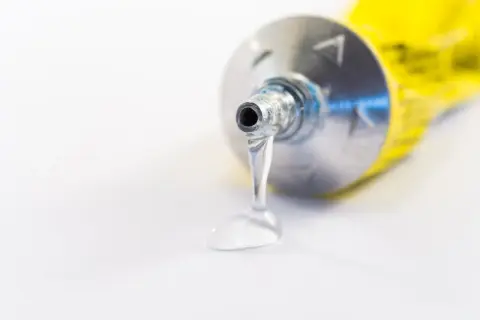 Kropla przezroczystego kleju wypływa z metalowej tubki. Idealne rozwiązanie, czym skleić plastik.