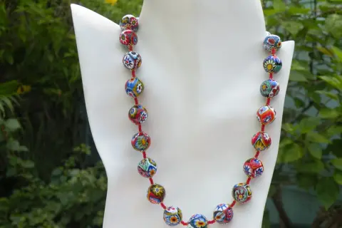 Colgantes de cristal de Murano, un collar vibrante con cuentas esféricas multicolores, cada una con un diseño floral único, sobre un fondo verde exuberante.