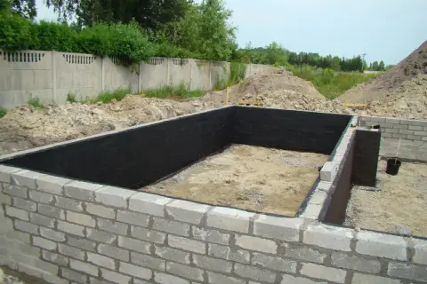 Fundament z bloczków betonowych, wewnątrz czarna izolacja. Widać kilka warstw bloczka fundamentowego.