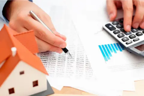 Man calculando el precio tasación vivienda con calculadora y modelo de casa.