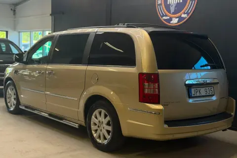 En gyllene Chrysler Voyager står parkerad. Den har en takbox och en svensk registreringsskylt.