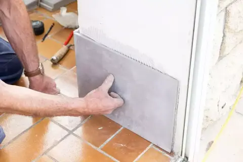 Pose d'un carrelage sur placo. Un artisan applique une plaque de carrelage gris sur un mur en placo, prêt à être collé.