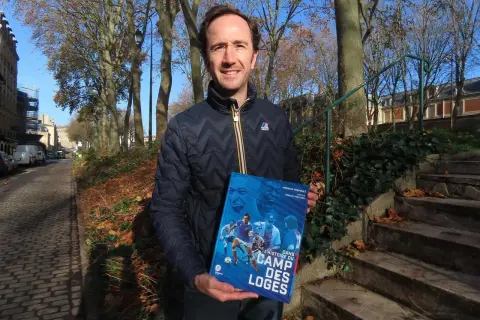 Un homme tient un livre intitulé "Dans l'histoire du Camp des Loges", avec des images de football sur la couverture.