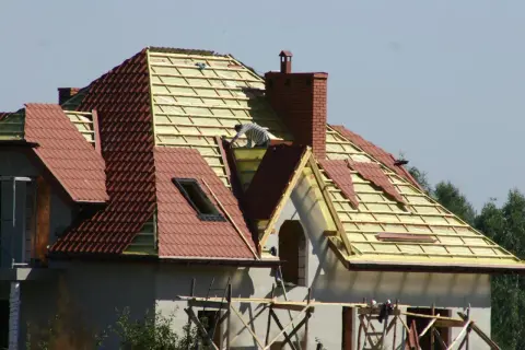 Budowa domu z czerwoną **attiką** i nowym dachem.