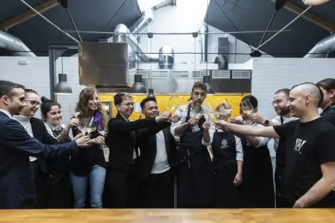 Equipo brindando con copas de vino en una cocina profesional, celebrando el éxito culinario que podría llevar a estrellas Michelin Zaragoza.