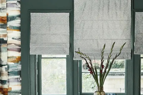 Tende a pacchetto grigie scintillanti fino al davanzale, accanto a una tenda con pennellate astratte colorate.