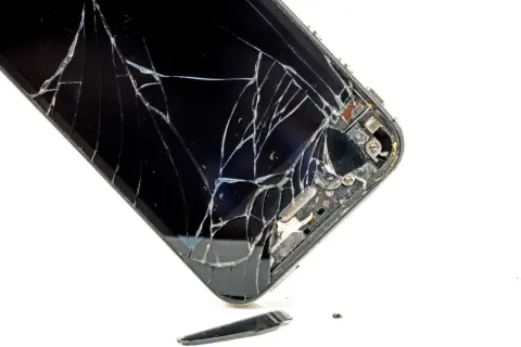 Rozbite szkło telefonu. Widać pęknięcia i fragmenty, które odpadły. To pokazuje, czym się różni szkło hartowane od hybrydowego w praktyce.