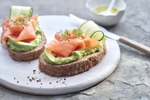 Deux toasts avocat saumon, garniture fraîche avec concombre et aneth, sur pain complet.