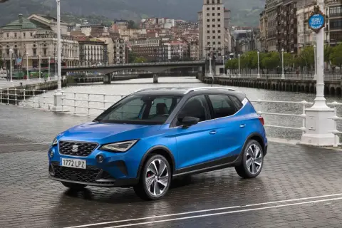 Blå Seat Arona parkerad vid en kaj med stad och broar i bakgrunden. Perfekt för en seat arona test i en europeisk stad.