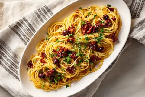 En skål med spaghetti, toppad med soltorkade tomater, oliver och persilja. En härlig pasta puttanesca.