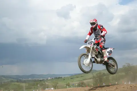 Motocrossowiec w skoku na motocyklu, podobnym do Husqvarna Motorcycles i KTM, w czerwono-białym stroju.