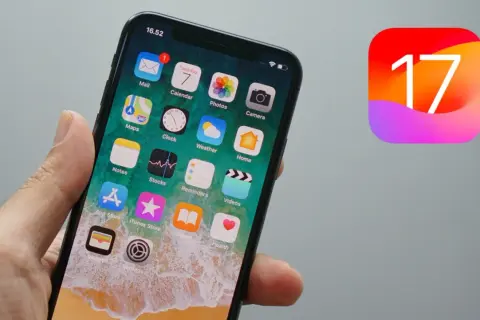 Dłoń trzyma iPhone'a z ikonami aplikacji, obok widnieje logo iOS 17.