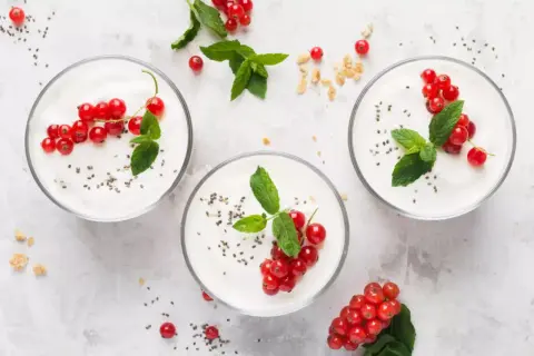 Trzy pucharki z jogurtem naturalnym, udekorowane porzeczkami i miętą. Zastanawiasz się, ile cukru ma jogurt naturalny? Ten jest pyszny i zdrowy!
