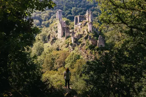 Une personne contemple les ruines d'un château perché sur une colline boisée. Une belle idée de que faire en Corrèze pour les amateurs d'histoire et de nature.