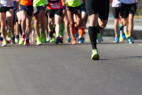 Gambe di corridori in maratona, con scarpe colorate. Un esempio di tabella maratona 4 allenamenti settimanali.