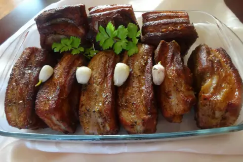 Pyszne żeberka w miodzie, pieczone z czosnkiem i natką pietruszki, prezentują się apetycznie na szklanej tacy.
