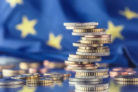 Stos monet euro na tle flagi UE symbolizuje pomoc de minimis dla przedsiębiorców.