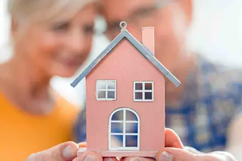 Un couple regarde une maison miniature rose, symbolisant leur recherche d'un logement senior pas cher pour leur avenir.