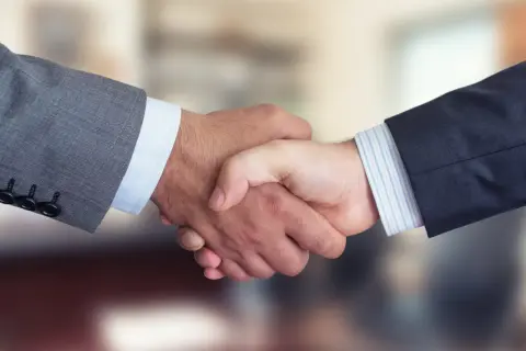 Dwaj mężczyźni w garniturach ściskają sobie dłonie, symbolizując udane joint venture i partnerstwo biznesowe.