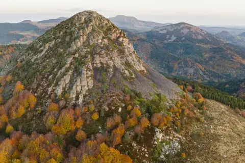 Vue aérienne du Mont Gerbier de Jonc en automne, ses pentes rocheuses et ses forêts aux couleurs flamboyantes. Une carte visuelle de ce paysage volcanique.