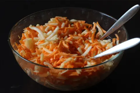 Schüssel mit geriebenen Karotten und Äpfeln, bereit für ein leckeres karottensalat rezept. Zwei Löffel warten darauf, den Salat zu servieren.