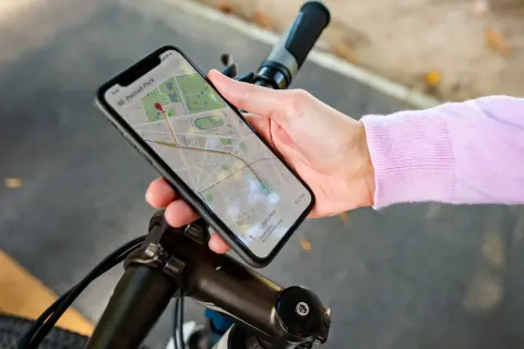 Dłoń trzyma smartfon z mapą, wskazującą trasę rowerową. Telefon pełni rolę licznika na rower, pokazując drogę do celu.