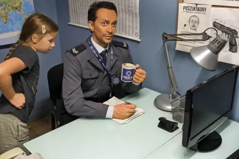 W muzeum Ojca Mateusza dziewczynka przygląda się woskowemu policjantowi z kubkiem "POLICJA".