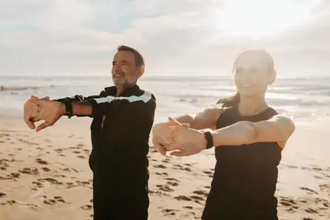 Para ćwiczy na plaży, ciesząc się słońcem i morzem. Idealne miejsce na turnusy rehabilitacyjne nad morzem.