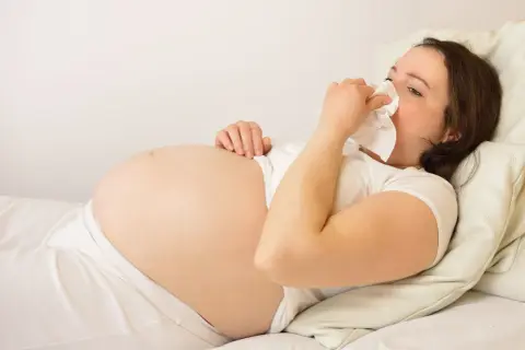 Gravid kvinna med andfåddhet ligger i sängen och snyter sig i en näsduk.