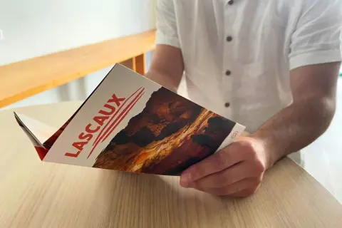 Un homme lit un dépliant sur la grotte de Lascaux, planifiant son itinéraire pour découvrir les peintures préhistoriques.