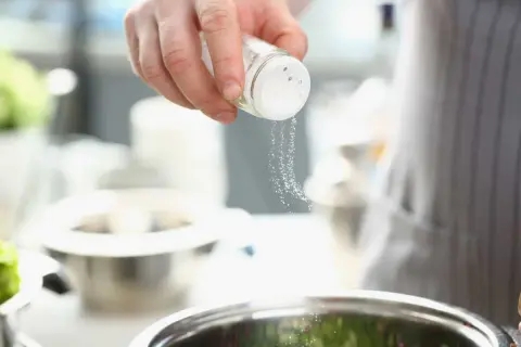 Une main saupoudre du sel dans un bol, ajoutant une touche de saveur à la cuisine.