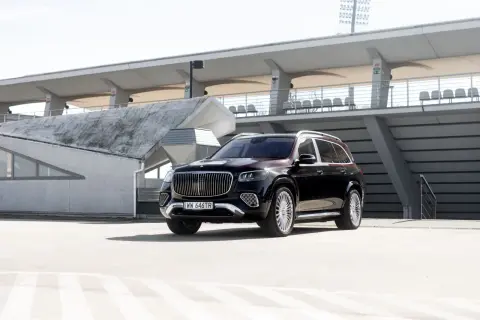 Elegancki, czarny Mercedes GLS Maybach z chromowanymi detalami i charakterystycznym grillem, zaparkowany na tle nowoczesnej architektury stadionu.