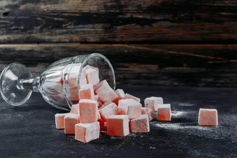 Un verre renversé d'où tombent des cubes de loukoum roses saupoudrés de sucre glace.