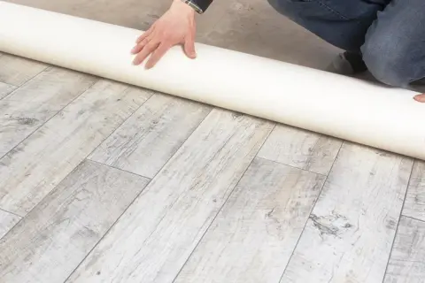 Eine Rolle Unterlage liegt auf einem Holzboden. Sie ist ideal, wenn Sie sich fragen, was kommt unter PVC Boden.