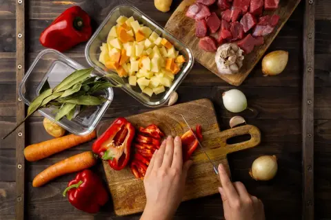 Przygotowania do pysznego **cheat meal**: krojenie papryki, mięso, ziemniaki, marchew, cebula, czosnek i liście laurowe.